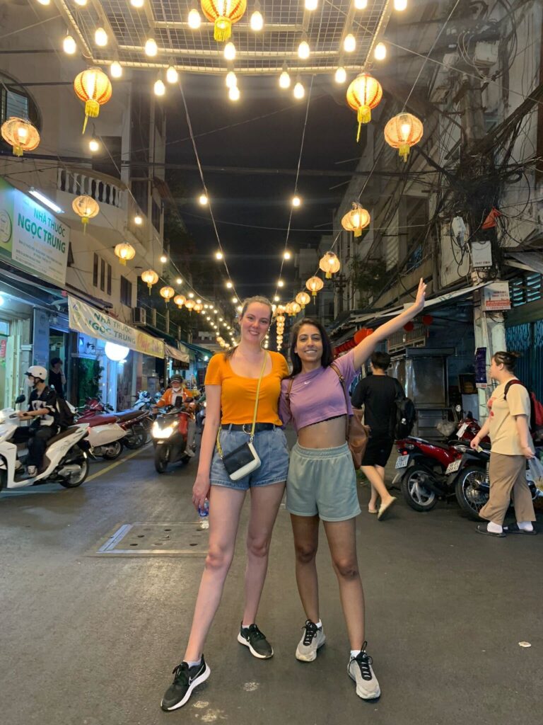 Gabby and Shivani remote working in Vietnam with festoon lighting behind them